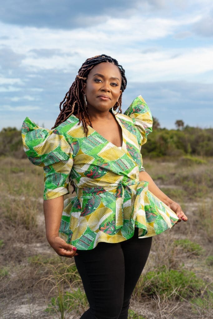 African American woman wearing McCalls 8146 pattern in green Ankara in an open field