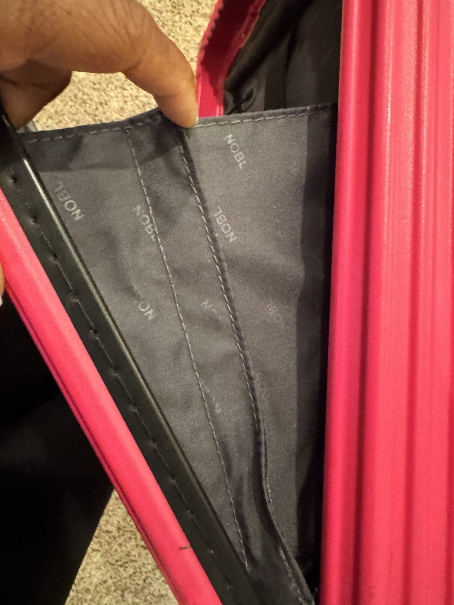 Scuffed silver aluminum handle on a pink NOBL suitcase